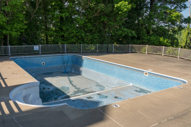 Technician resurfacing worn backyard pool finish before family returns for weekend swimming